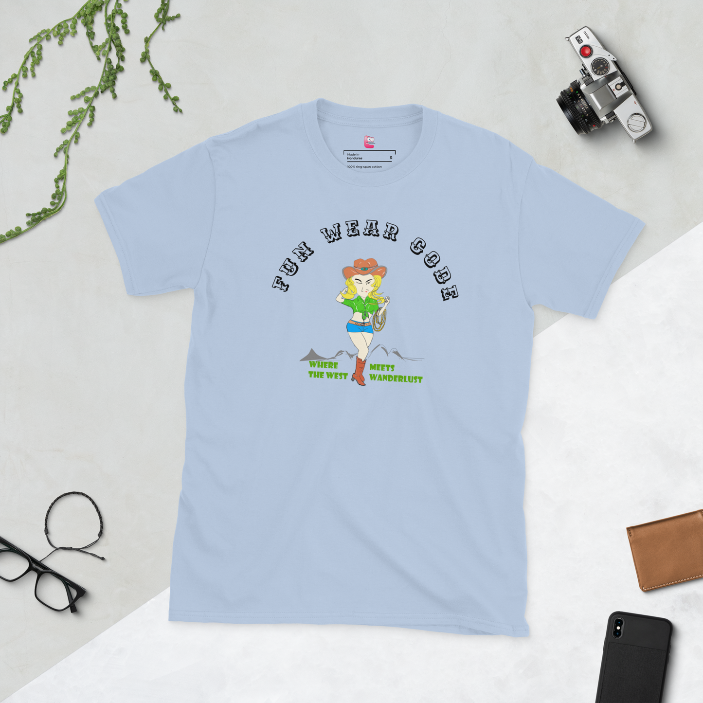 Light blue t-shirt with a graphic design of a cowgirl and text " FUN WEAR CODE" on a light gray surface with accessories around
