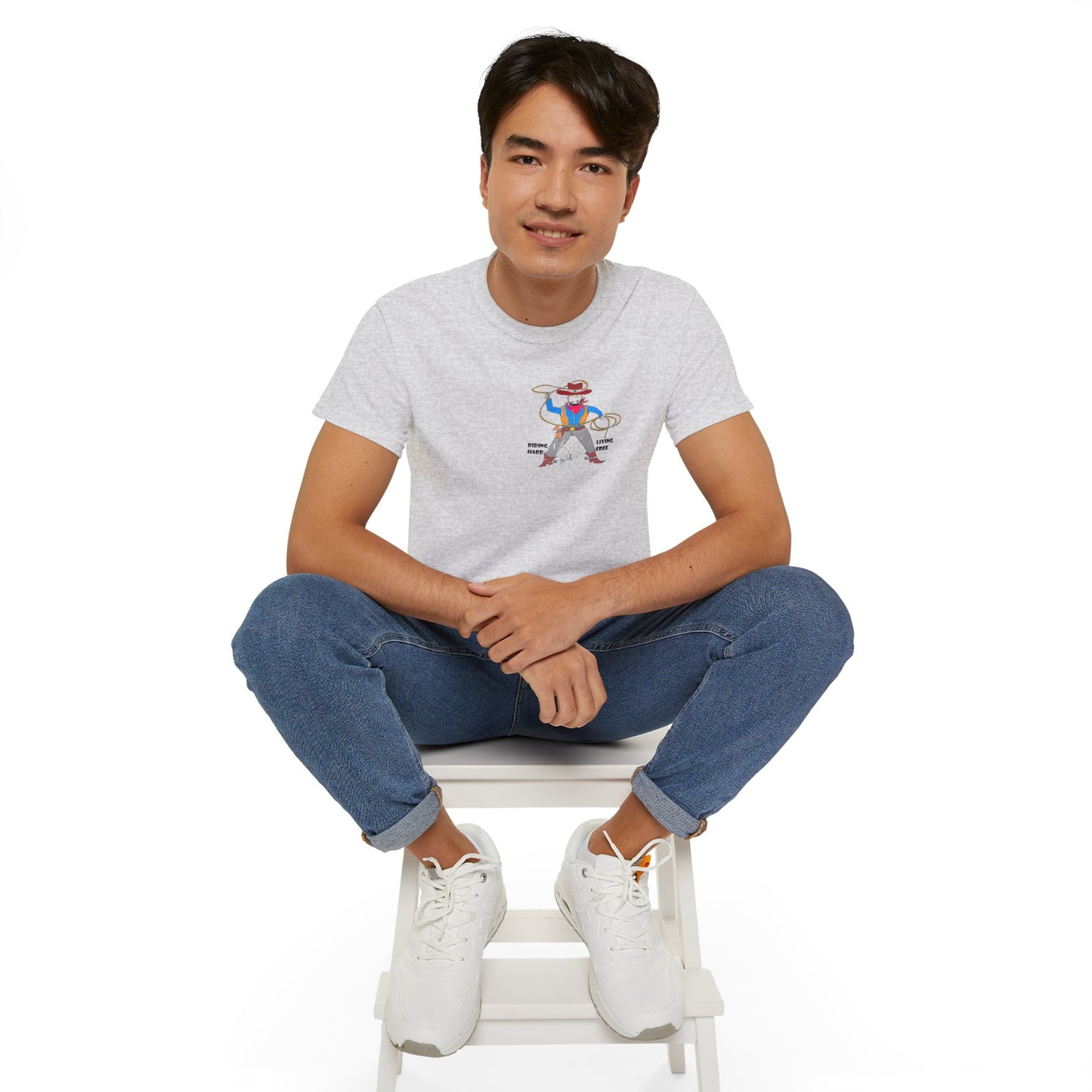 Front view of a man model wearing a gray t-shirt with a cowboy graphic design, sitting on a white stool against a white background
