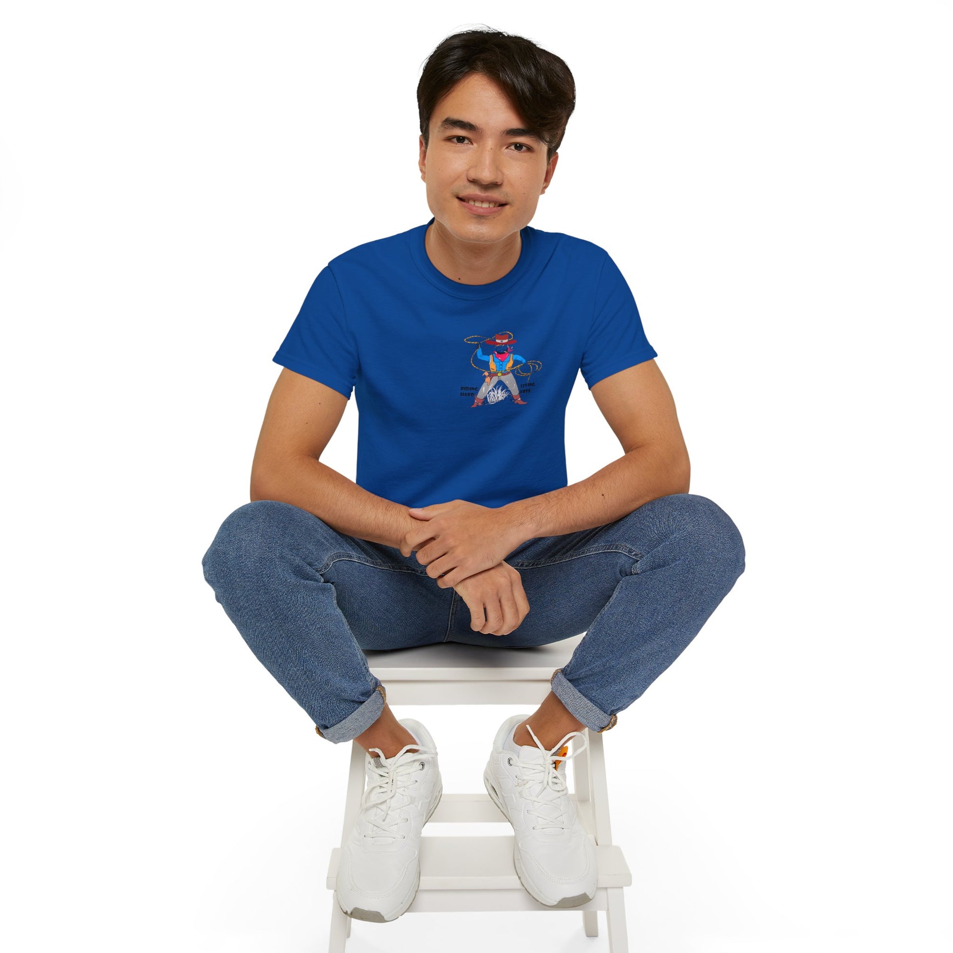 Front view of a man model wearing a blue t-shirt with a cowboy graphic design, sitting on a white stool against a white background