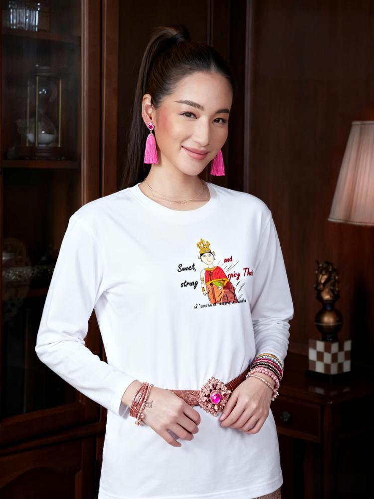 Woman wearing a white long-sleeve shirt with a playful Thai lady graphic and text "fun wear code", standing in an indoor setting.