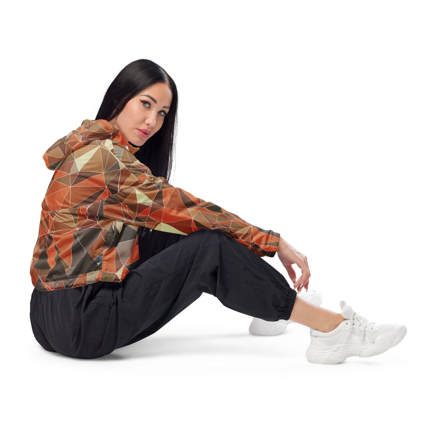 Woman wearing a cropped multicolor geometric patterned windbreaker jacket and black pants sitting on a white background