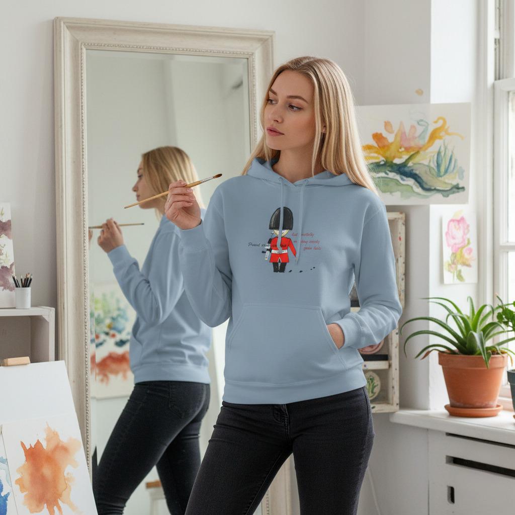 Woman wearing a blue hoodie with an English guardsman graphic design, standing in a room with art supplies and plants.