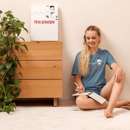 Woman wearing a judo themed T-Shirt, sitting on the floor reading a book with a wooden dresser and plant in the background