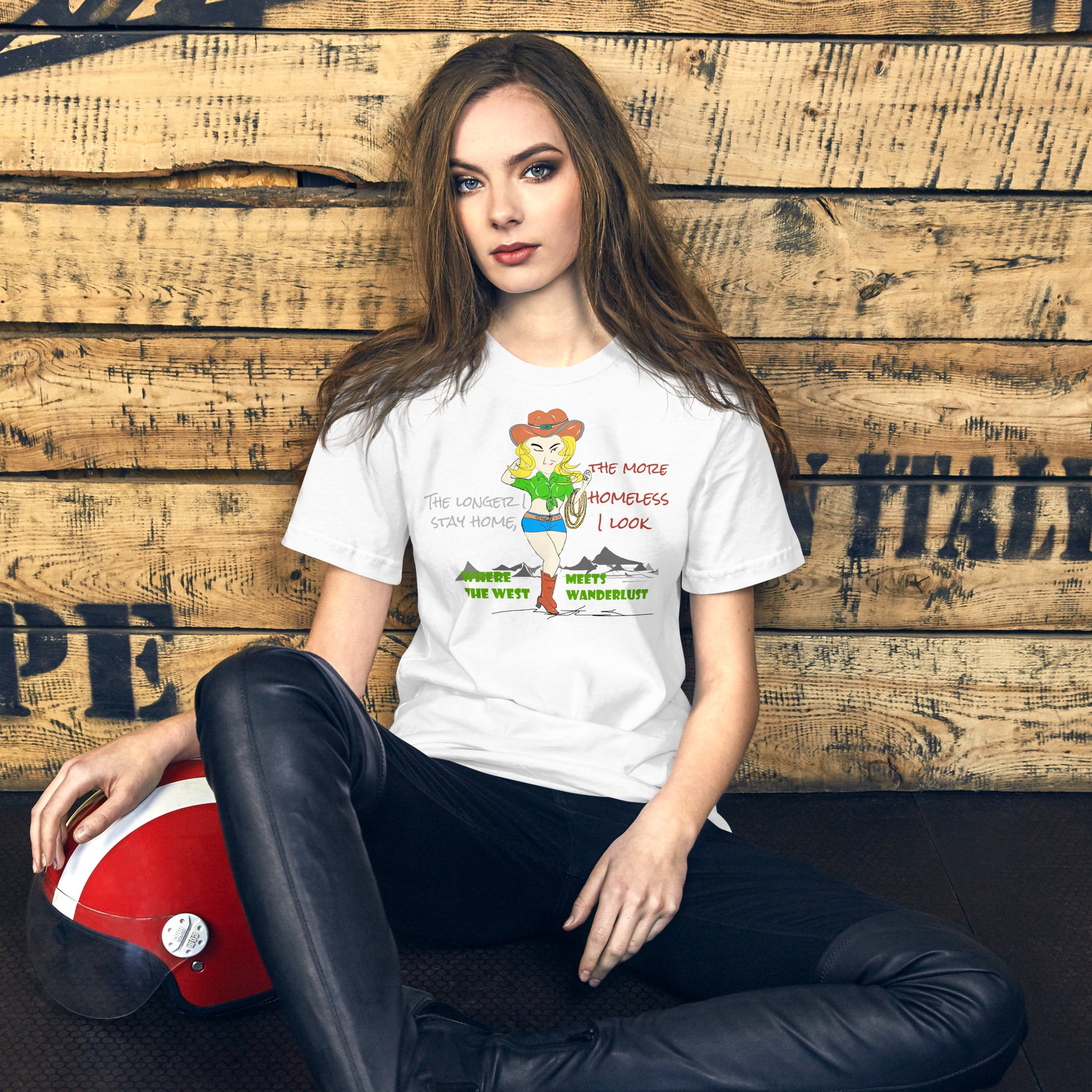 Woman wearing a white t-shirt with a playful cowgirl graphic design and text, sitting against a wooden wall.